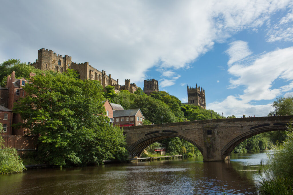 River with greenery and Durham castle and cathedral looming above.