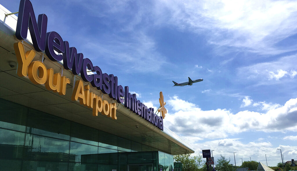 Newcastle International Airport terminal with plane flying overhead.