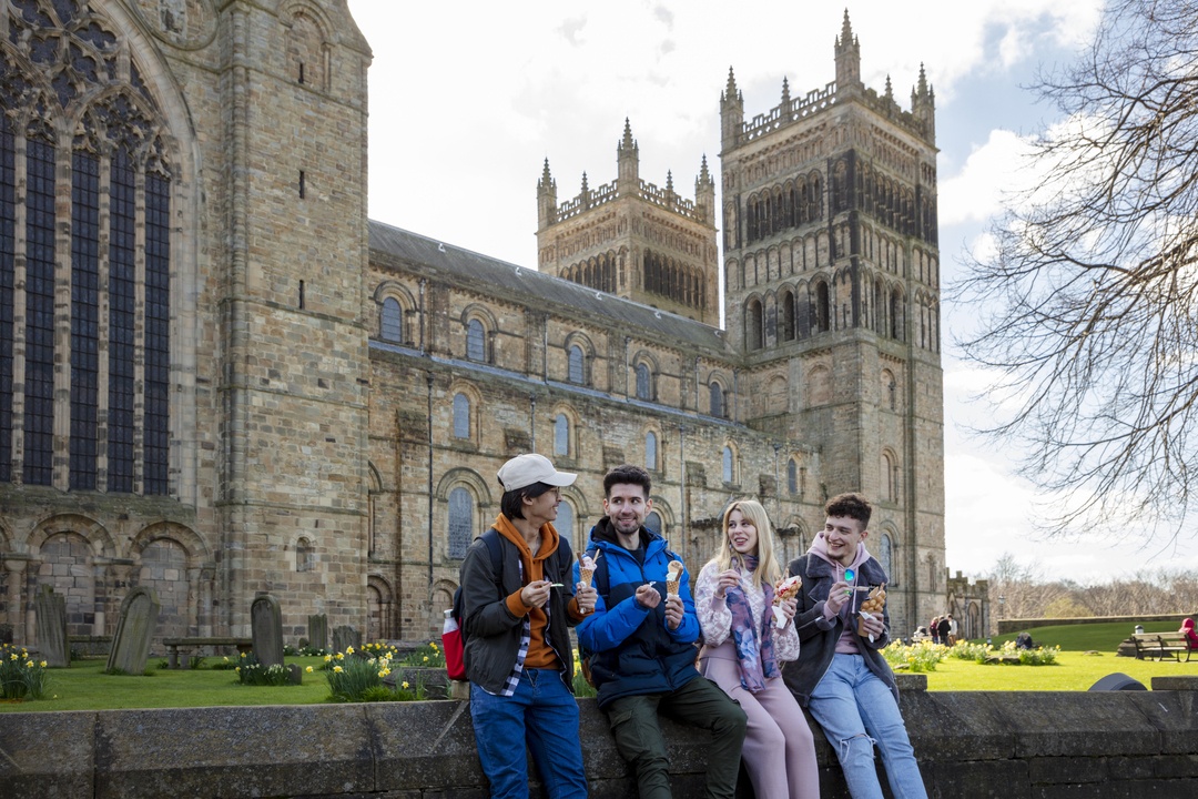 Four people sat along a wall in front of Durham Cathedral eating ice creams