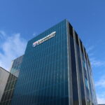 External shot of the Frederick Douglass Building at Newcastle University. The Newcastle University logo is in the middle of the glass fronted building and there is blue sky in the background.