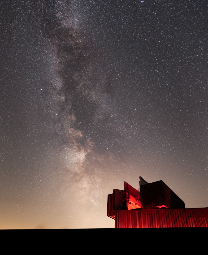 Image of Kielder Observatory at night lit up in a warm red light with a sky full of star up above.