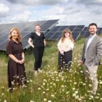 Four of the Newcastle Airport team stood in field of wildflowers with large solar panels lined up behind them.
